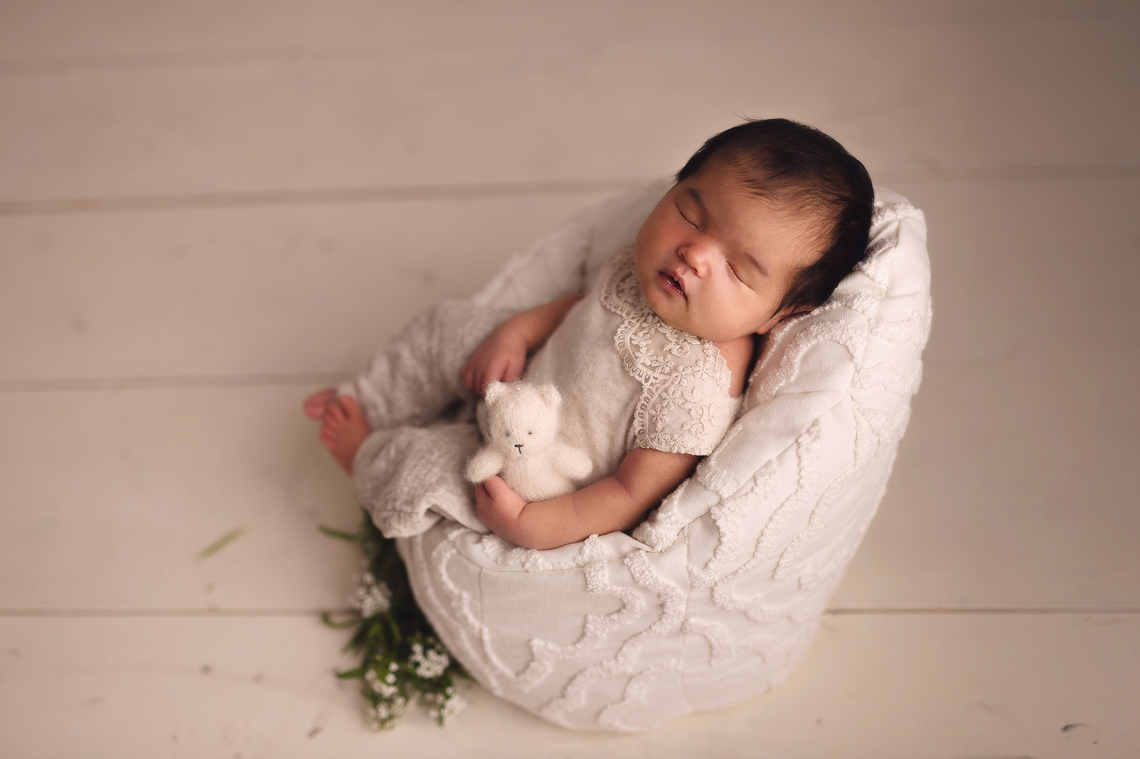 Newborn baby girl in the posing chair holding bear toy