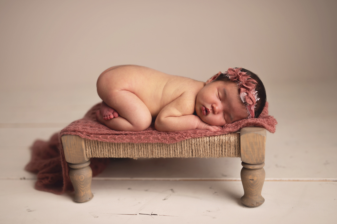 newborn baby girl sleeping on the hand made bench prop