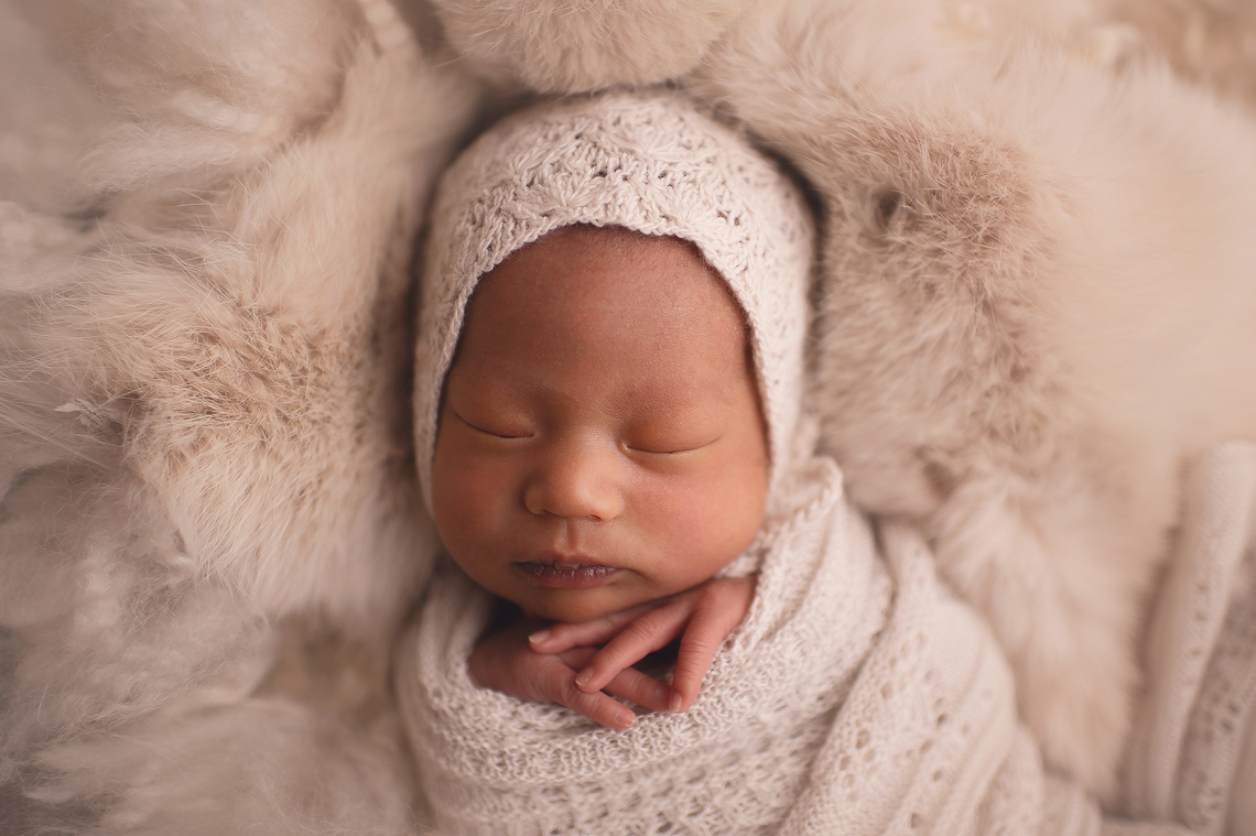 newborn baby girl lying on light fur wrapped with hands under the chin