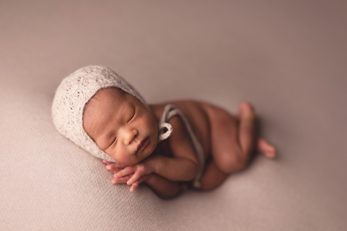 newborn baby girl lying on her side with both hands under her chin
