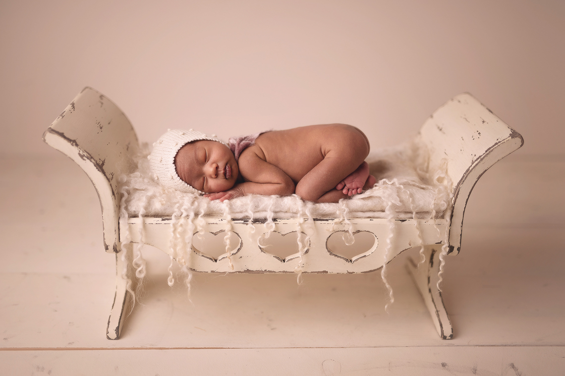 three week baby girl laying on her tummy on top of the wooden prop